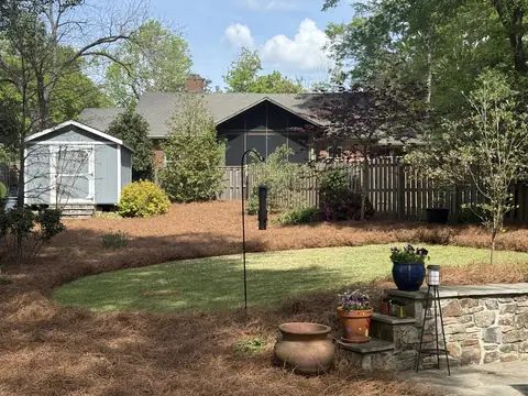 A backyard with fresh pine straw spread around a round lawn and a stone planter